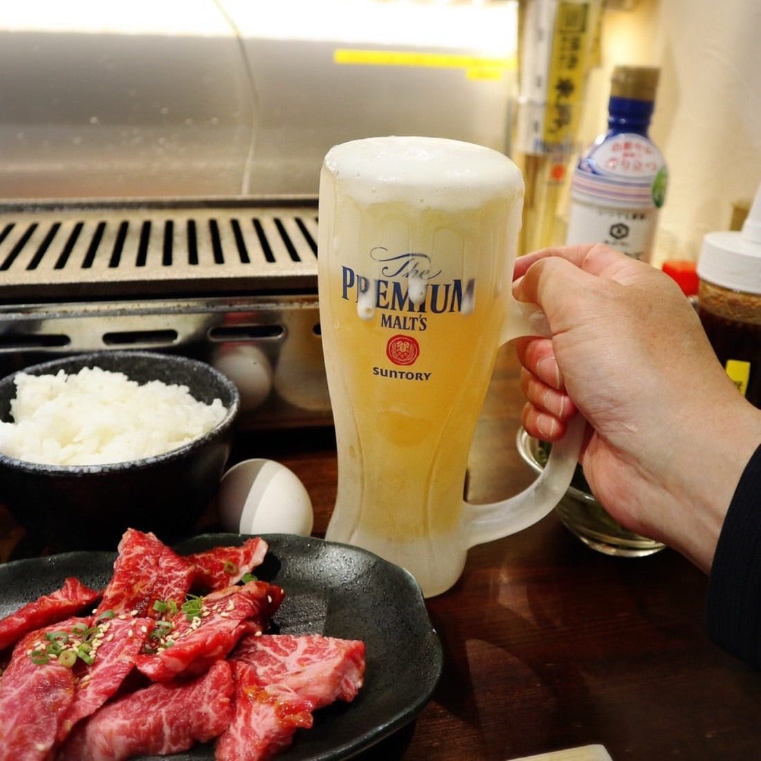 A grill built into the counter, with beef and a draft beer